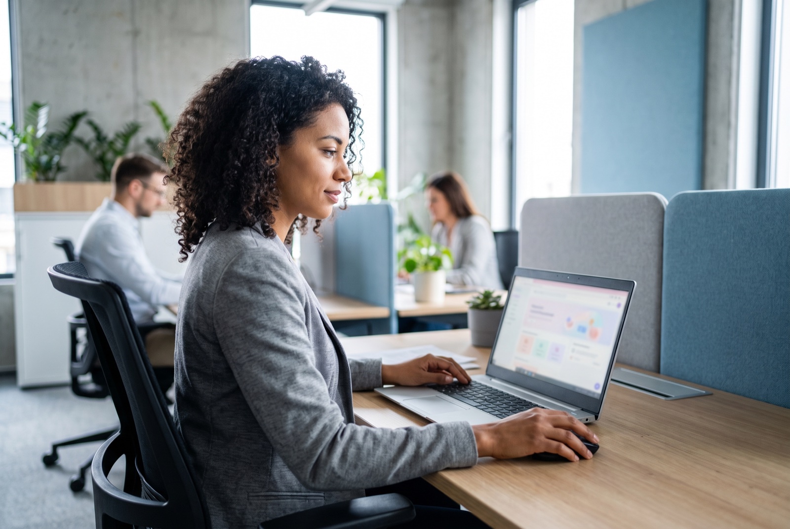 Localization specialist wearing headphones at a workstation, focused while comparing audio tracks, diverse colleagues collaborating softly blurred in the background of a bright office