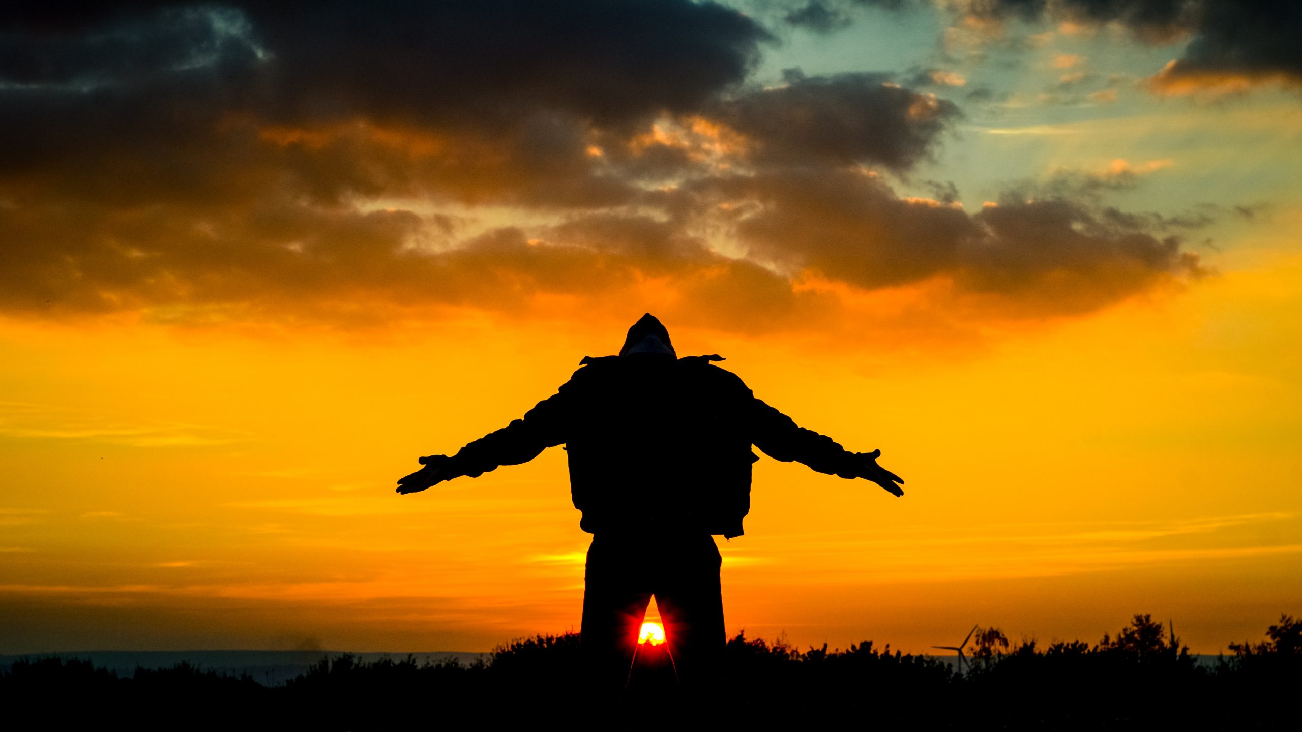 Silhouette of a person with arms outstretched against a vibrant sunset sky.