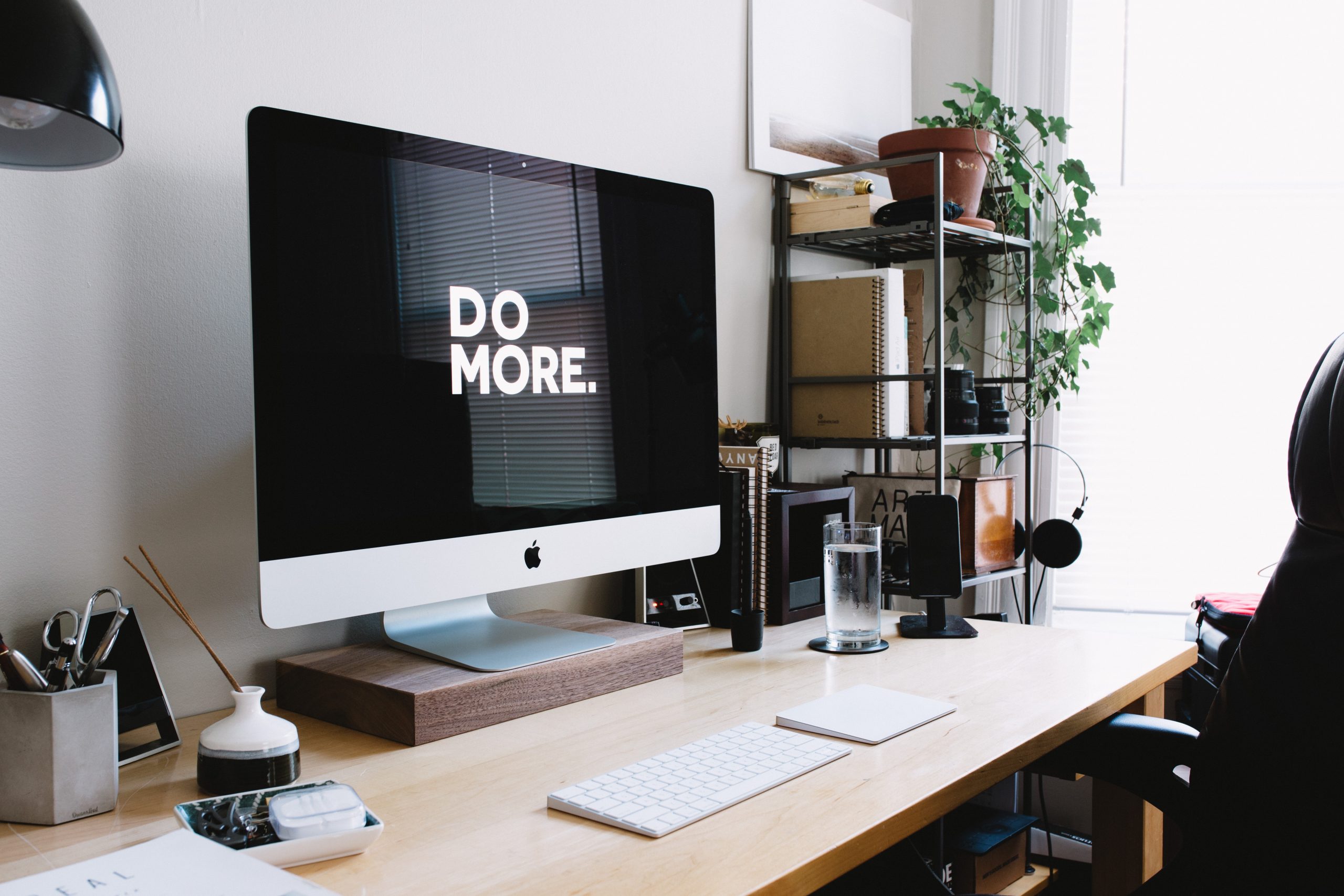 Modern workspace with 'DO MORE' on iMac screen, plant, and office supplies.