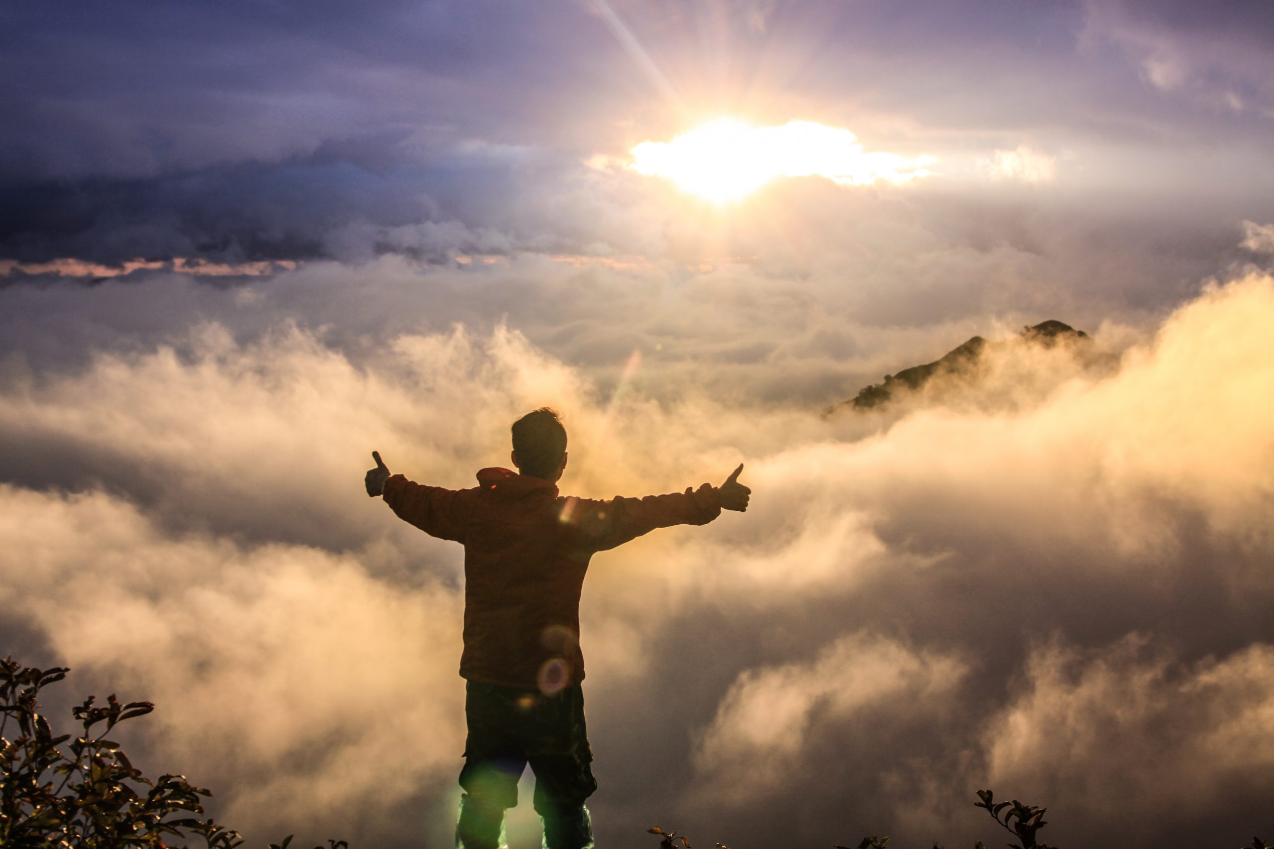 Person with arms raised above clouds at sunrise exuding success.