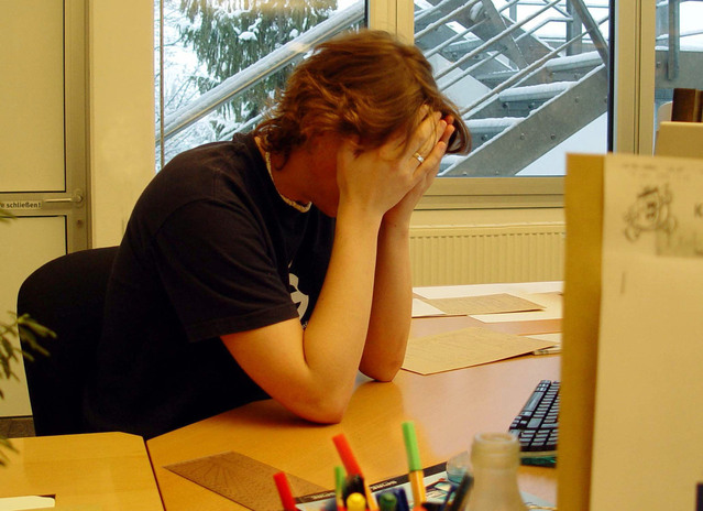 Stressed employee with head in hands at a cluttered office desk, indicating job burnout.