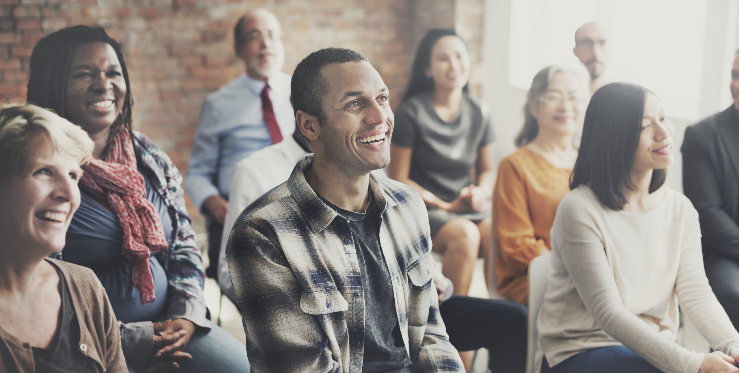 Diverse group of professionals smiling during a workshop with a brick wall background.