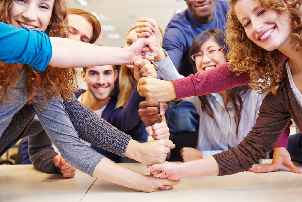 Diverse team stacking hands in unity, symbolizing teamwork and cooperation.