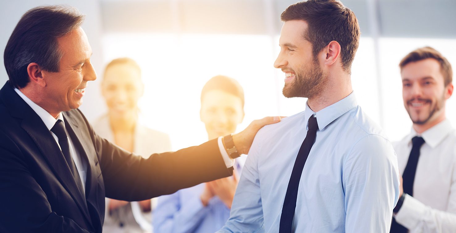 Senior executive shaking hands with smiling young professional in office.