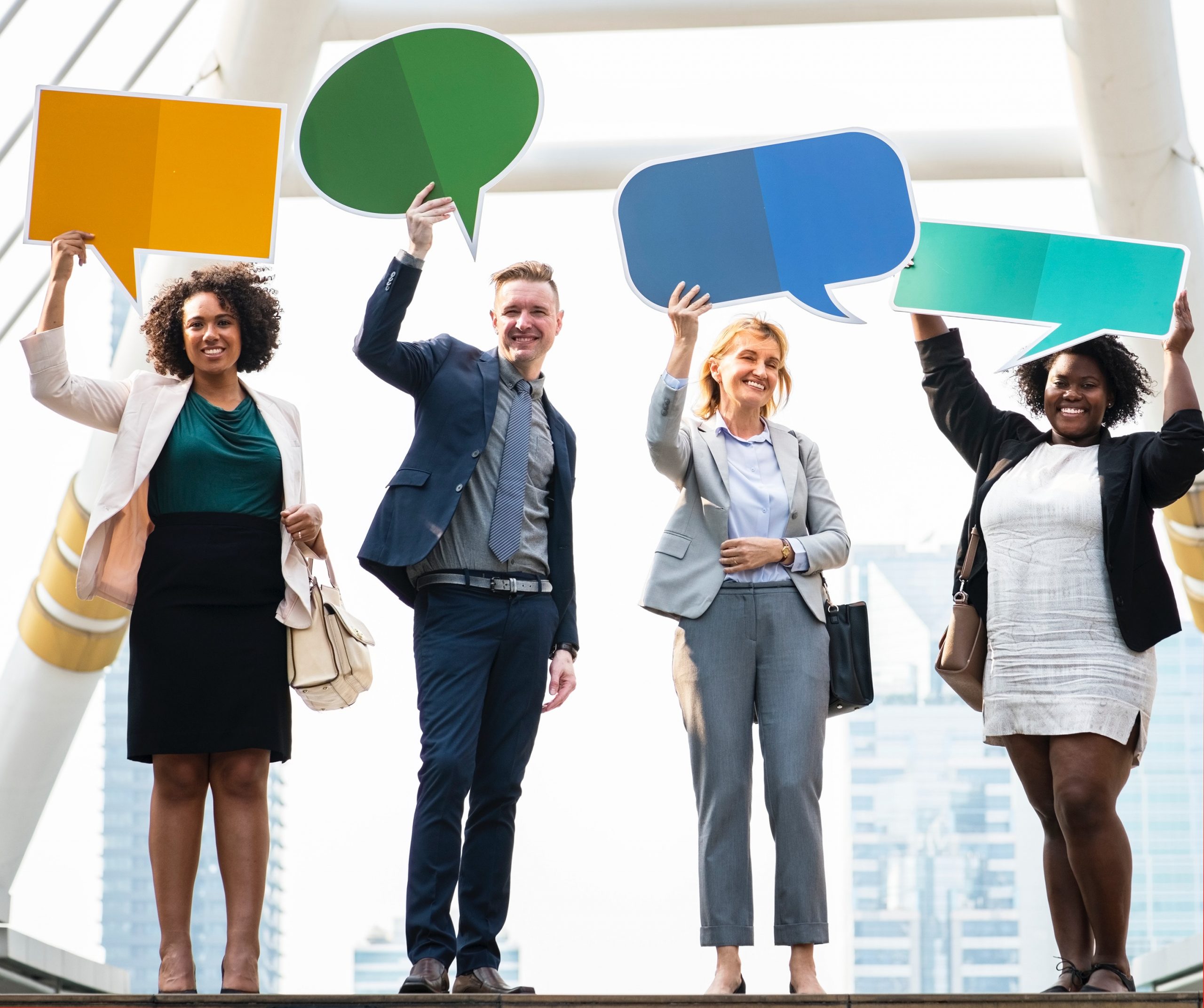 Four professionals holding colorful speech bubble signs overhead in a cityscape.