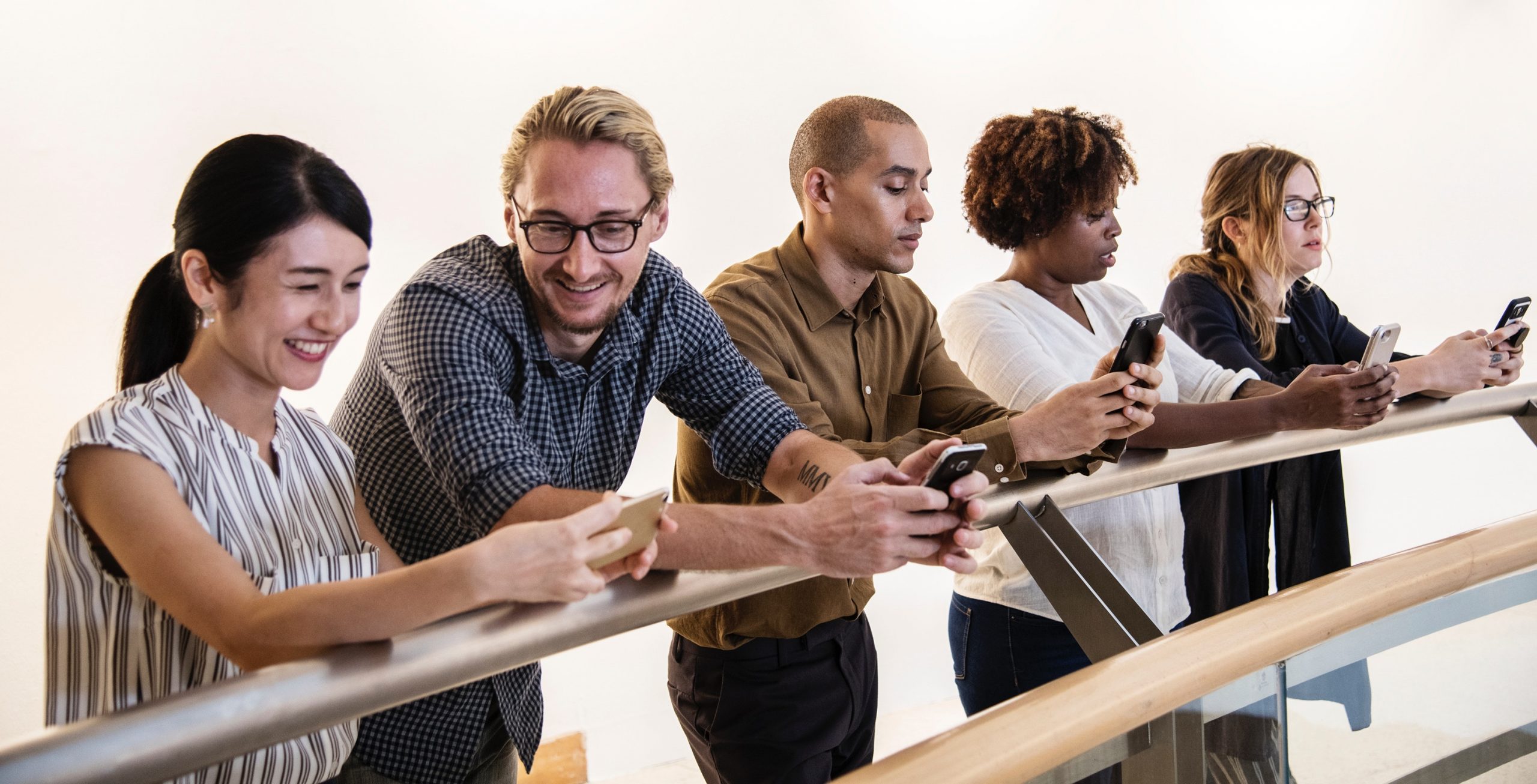 Diverse group of professionals using smartphones leaning on a railing in an office setting.