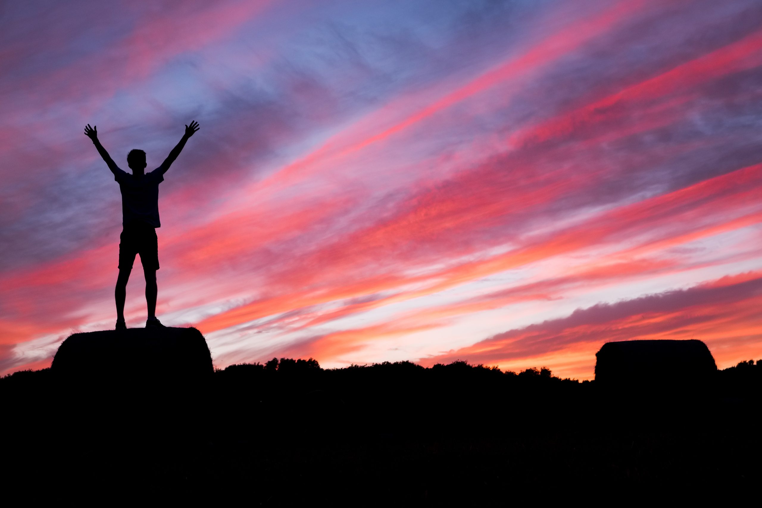 Silhouette of a person with arms raised against a vibrant sunset sky.