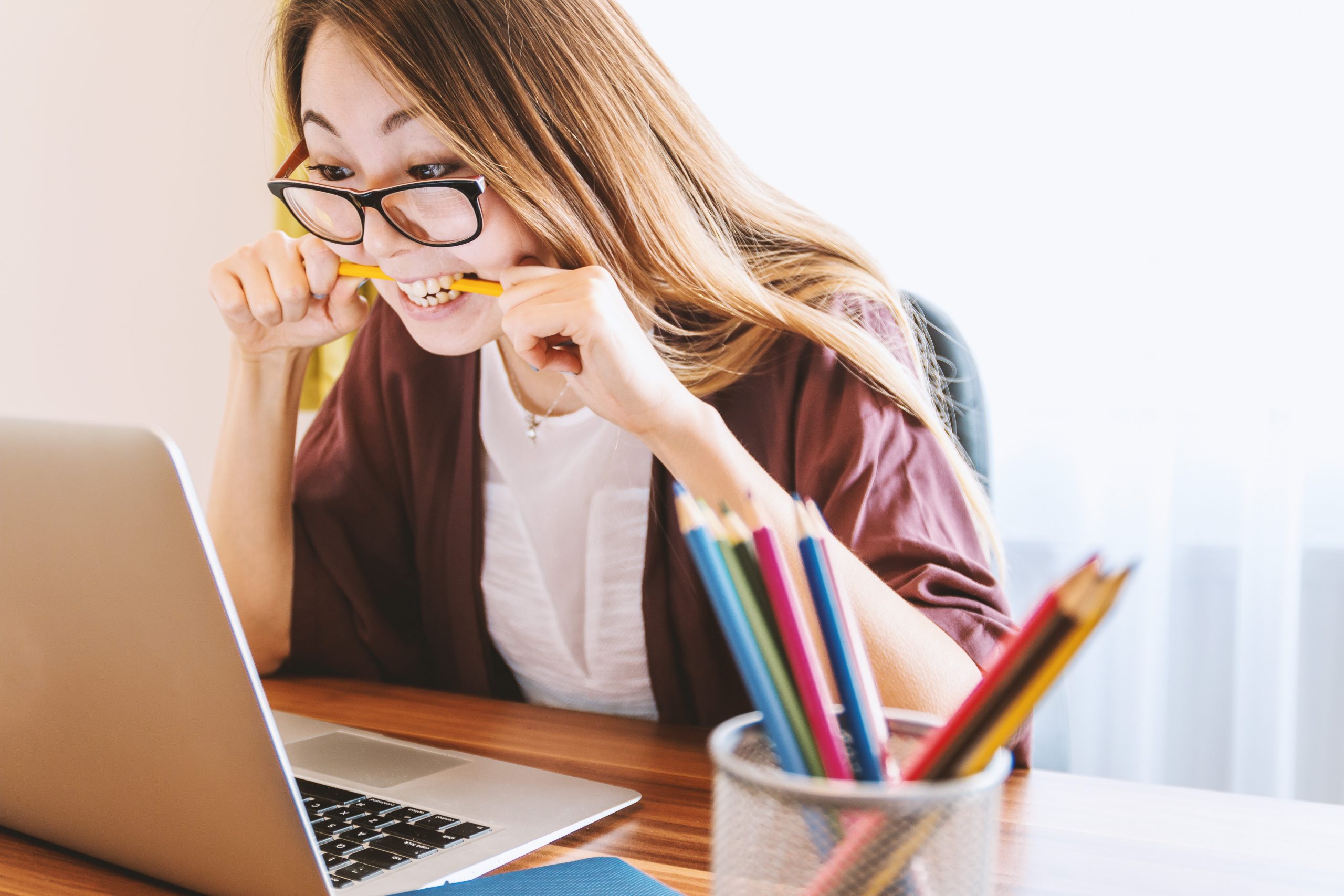 Focused woman biting pencil while working on laptop.