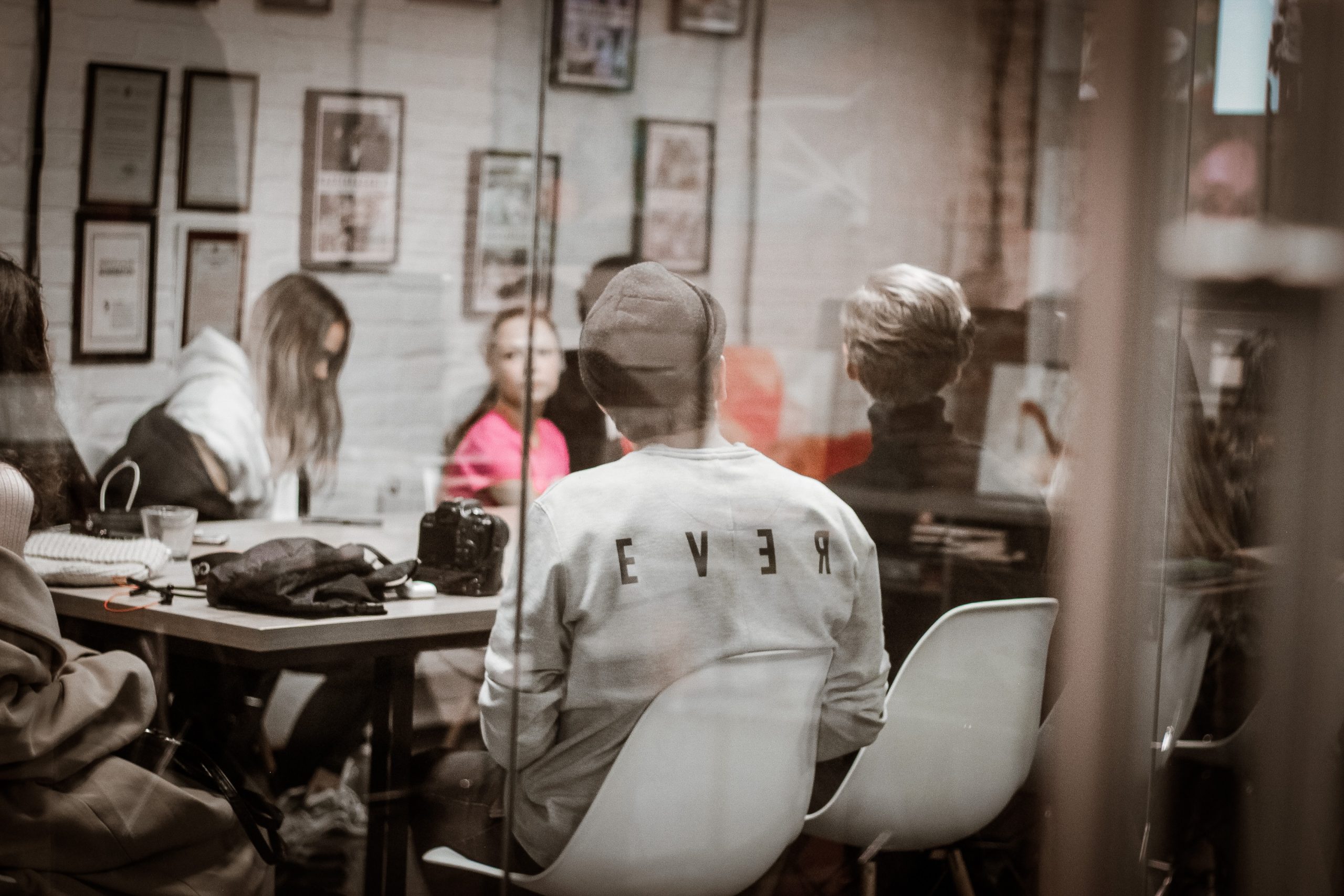 Person in beanie and 'REVER' shirt sitting with others at a busy workshop.