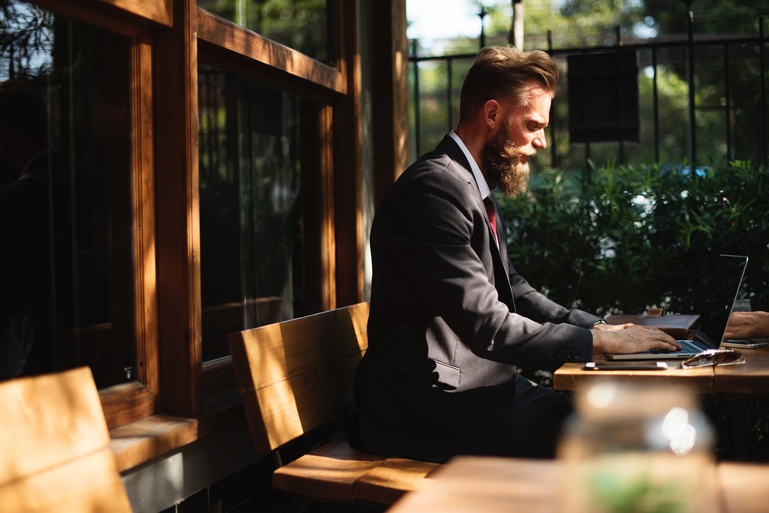 Focused businessman working on laptop at outdoor bench in sunlight.