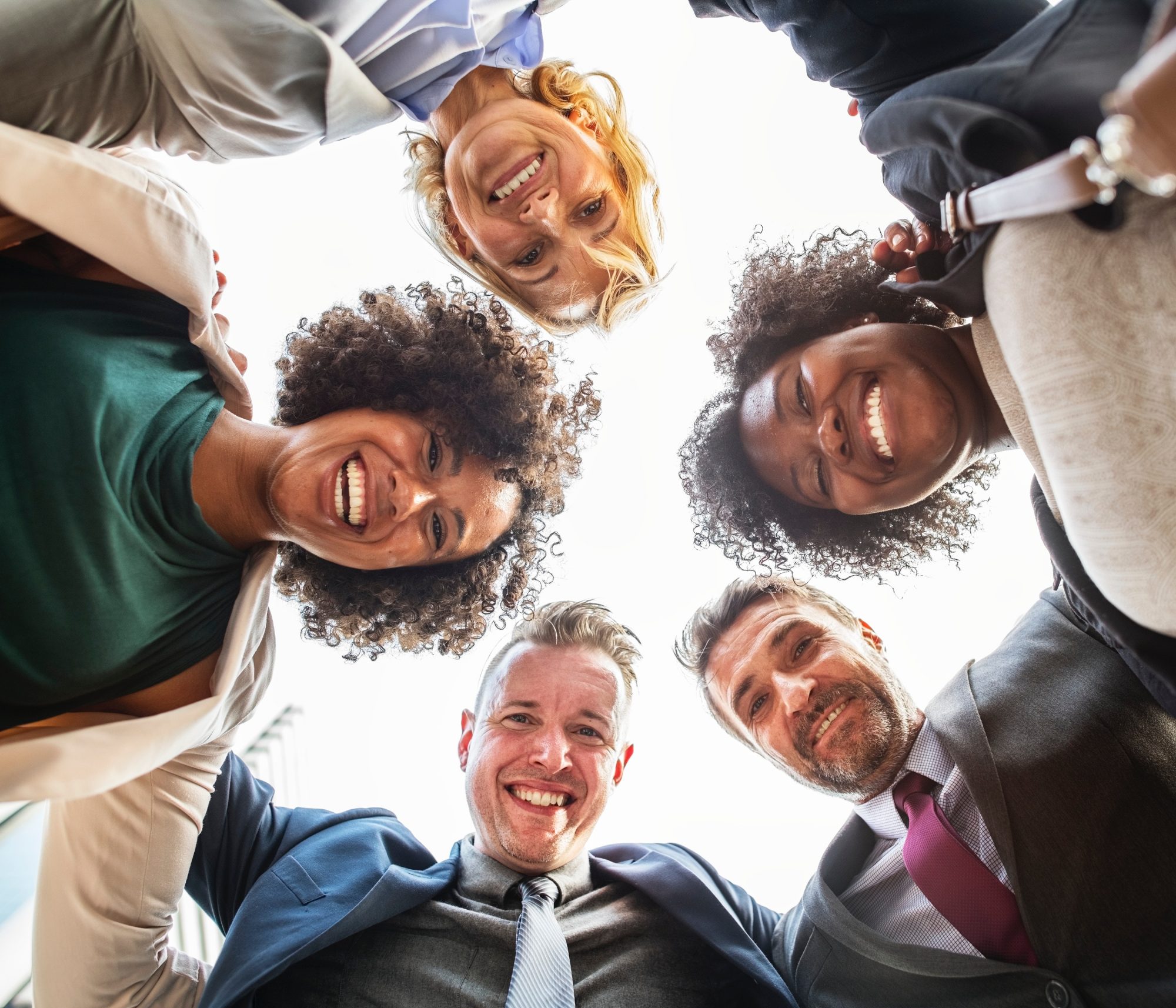 Diverse group of smiling colleagues in a huddle from below.