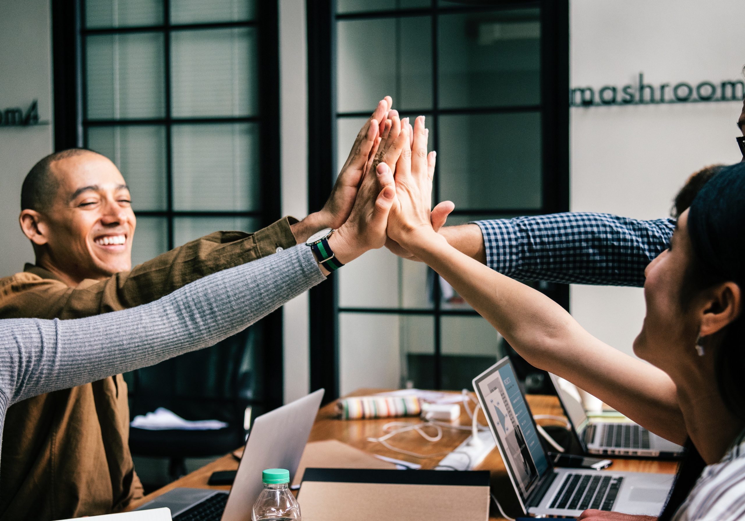 Cheerful coworkers giving a high-five over a work table with laptops.