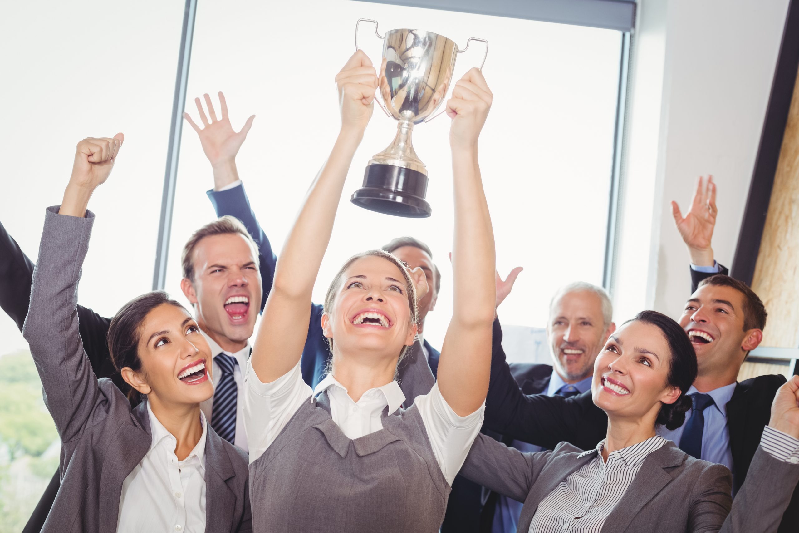 Ecstatic business team celebrating with trophy in an office setting.