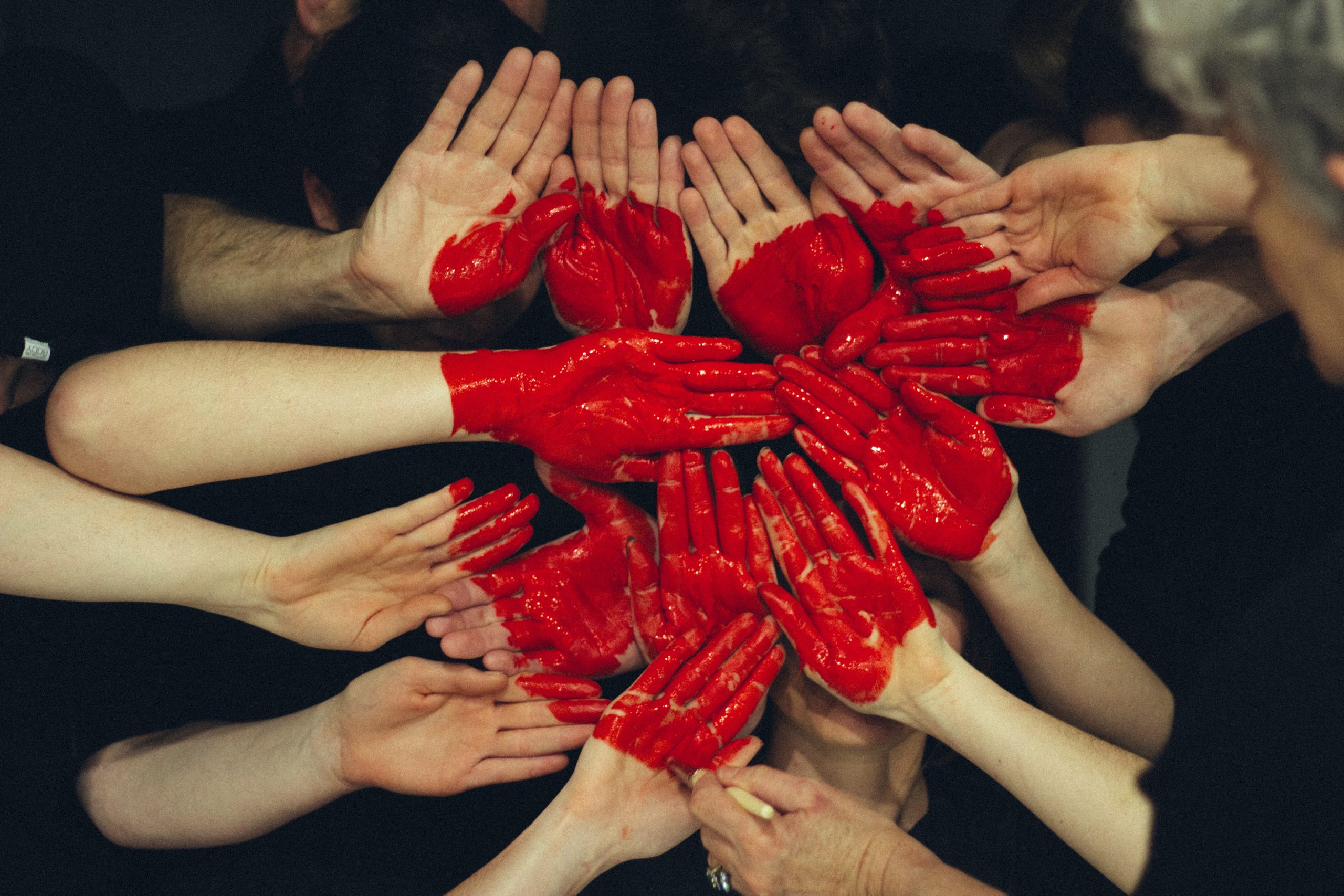 Group of hands together with red paint forming a heart shape.