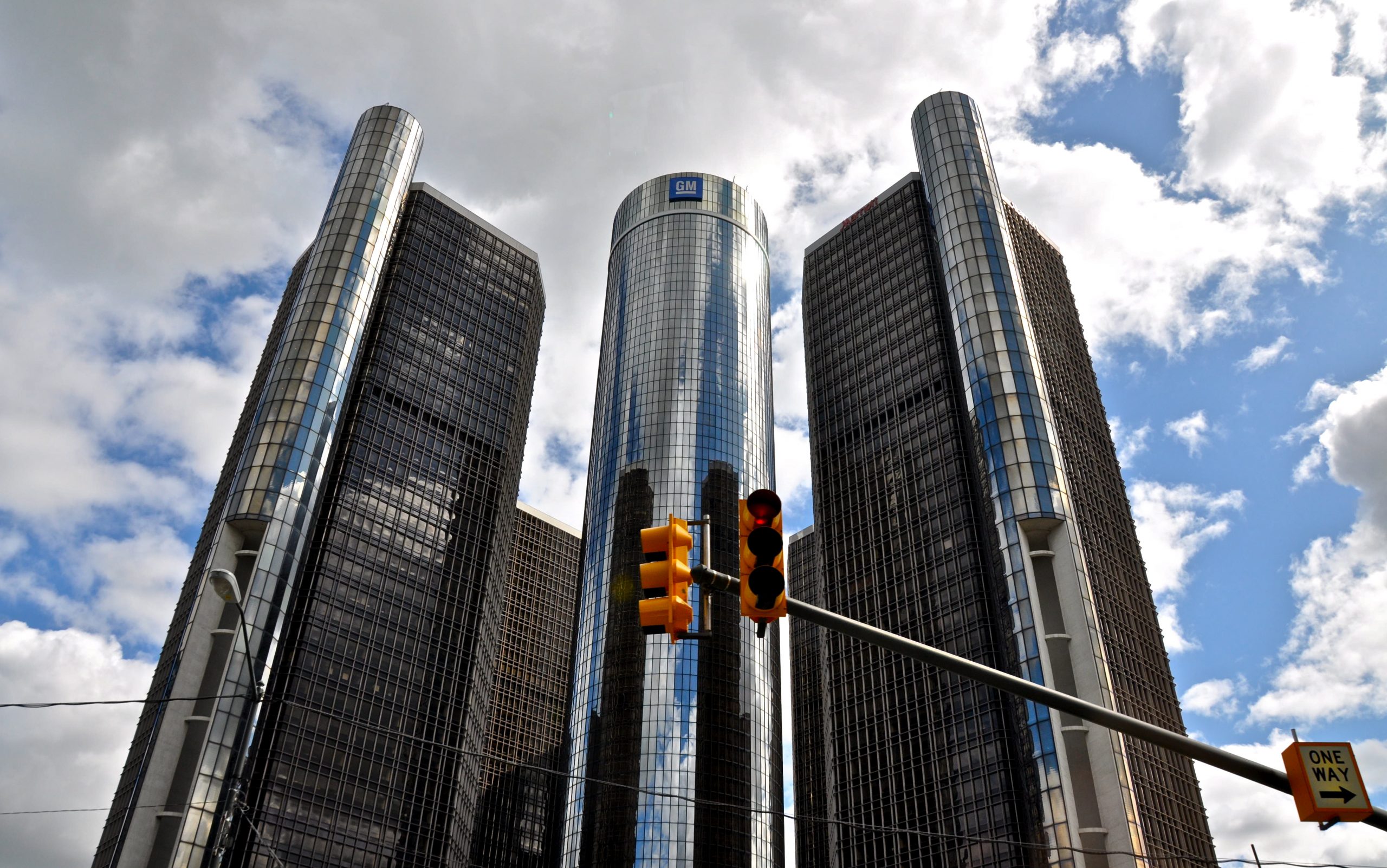 Modern skyscrapers with GM building under cloudy sky, traffic light in foreground.