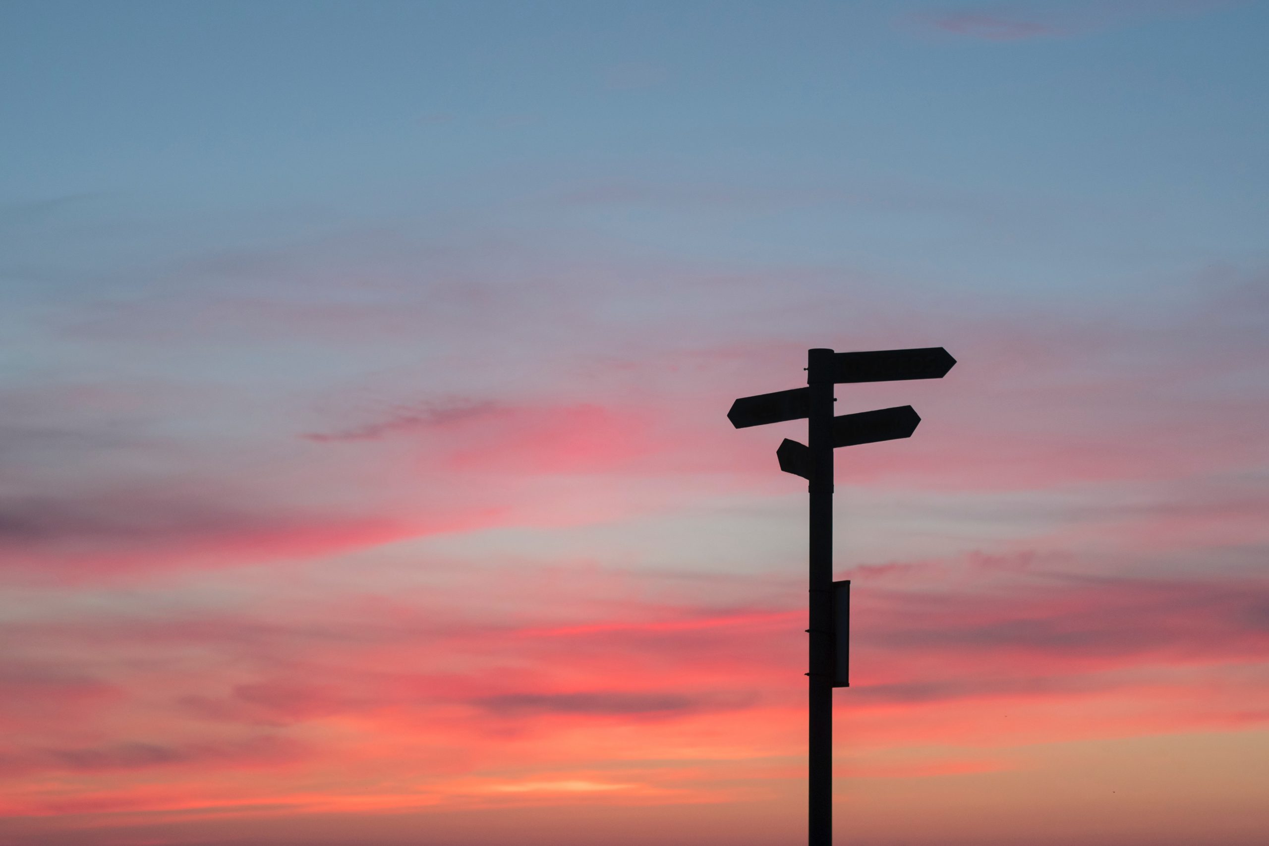 Blank direction signpost against a vibrant sunset sky.