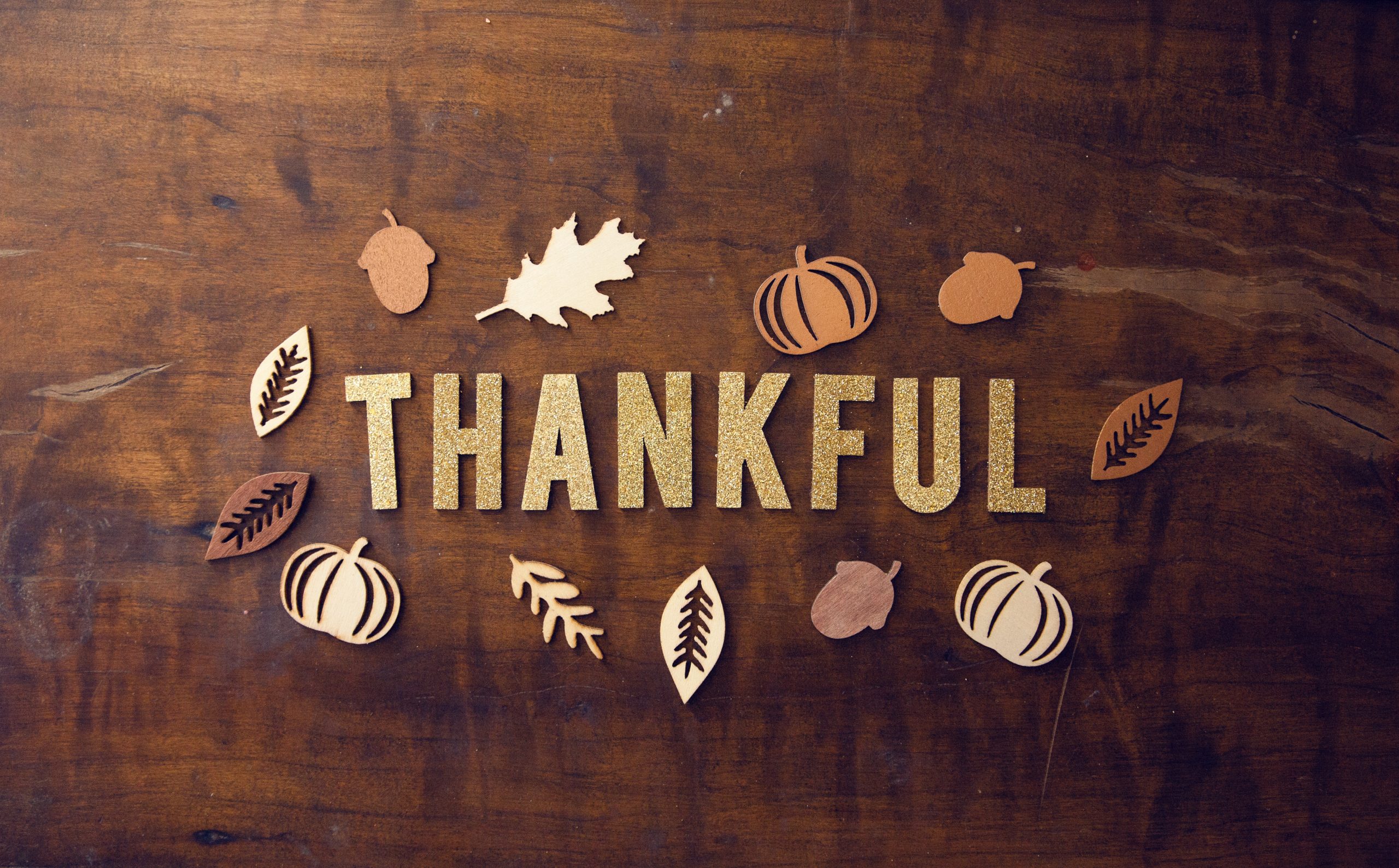 The word THANKFUL spelled out in glitter letters surrounded by autumn decorations on a wooden surface.