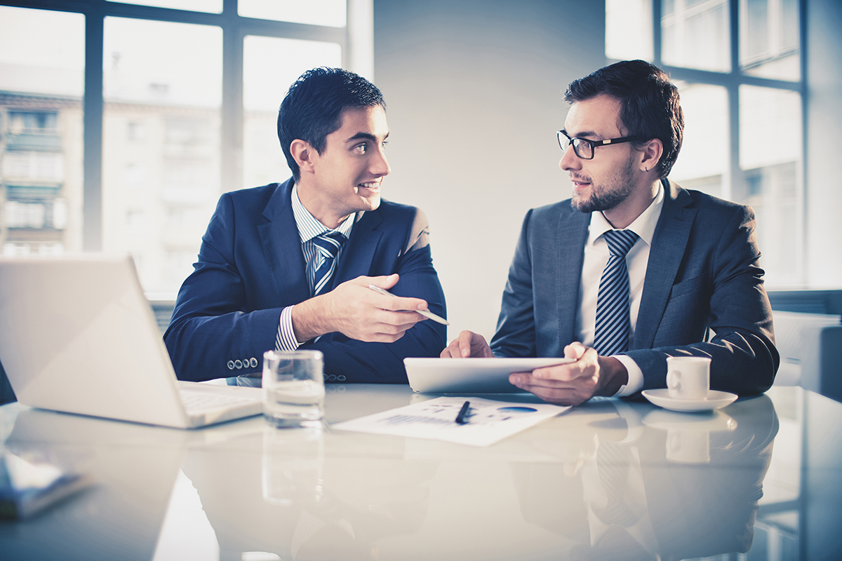 Two businessmen engaging in a discussion with digital tablet and laptop.