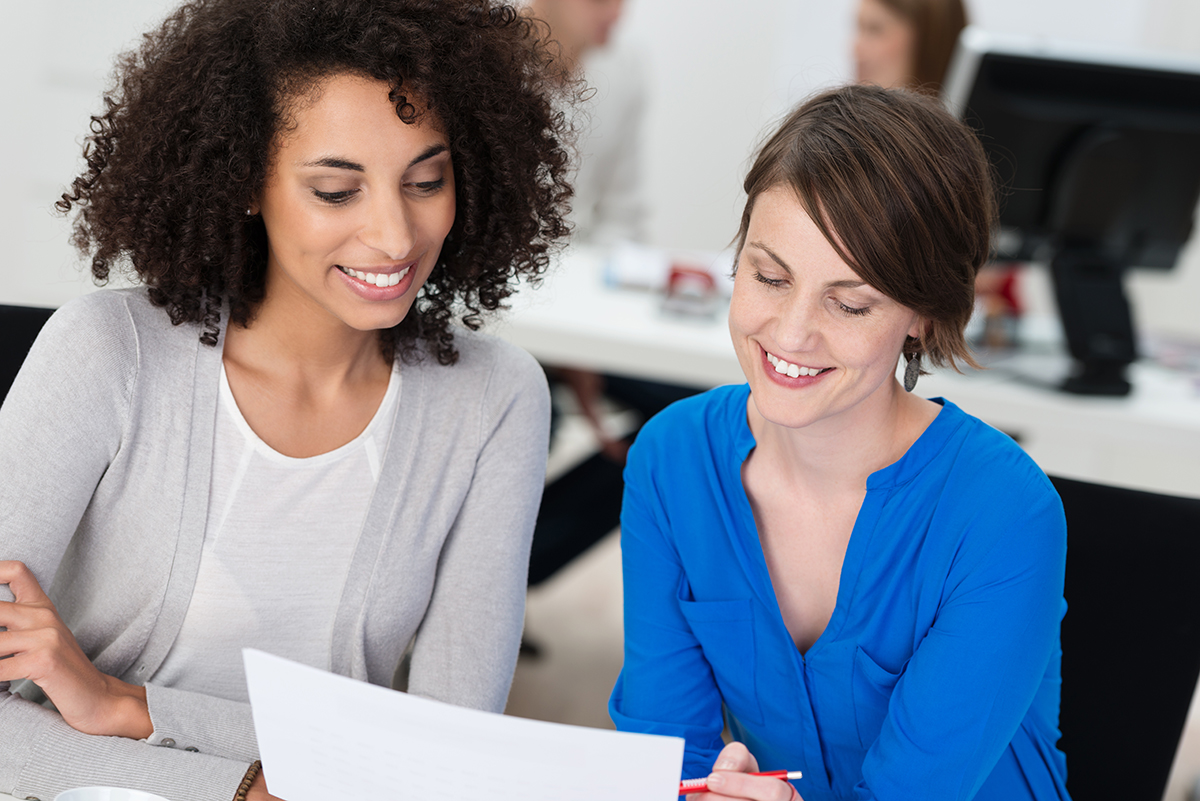 Two professional women collaborating with document in modern office setting.