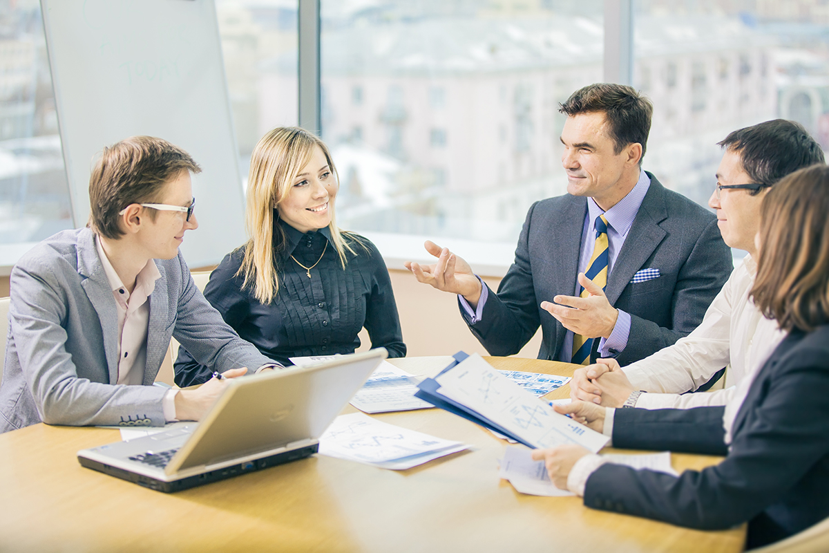 Diverse business team engaged in discussion with documents and laptop at a bright office table.