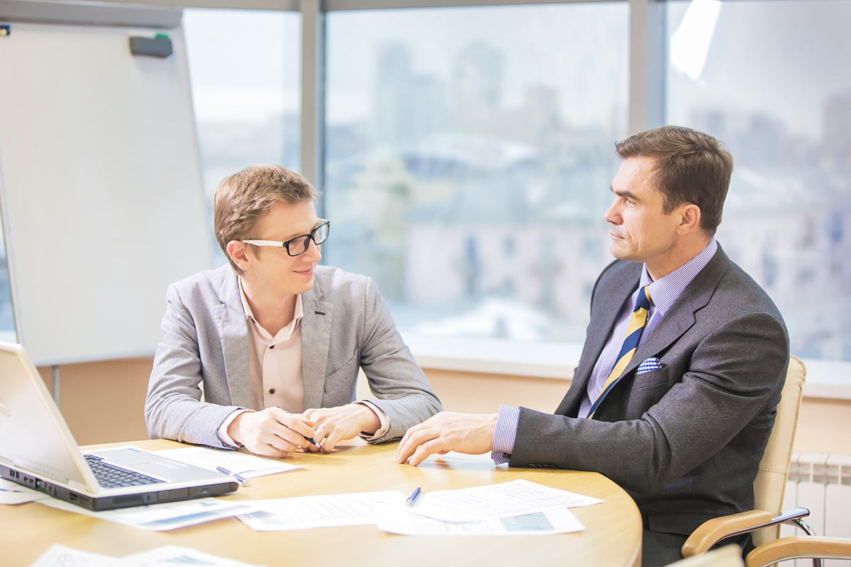 Two professionals engaged in a focused discussion with laptops and documents on a meeting table.