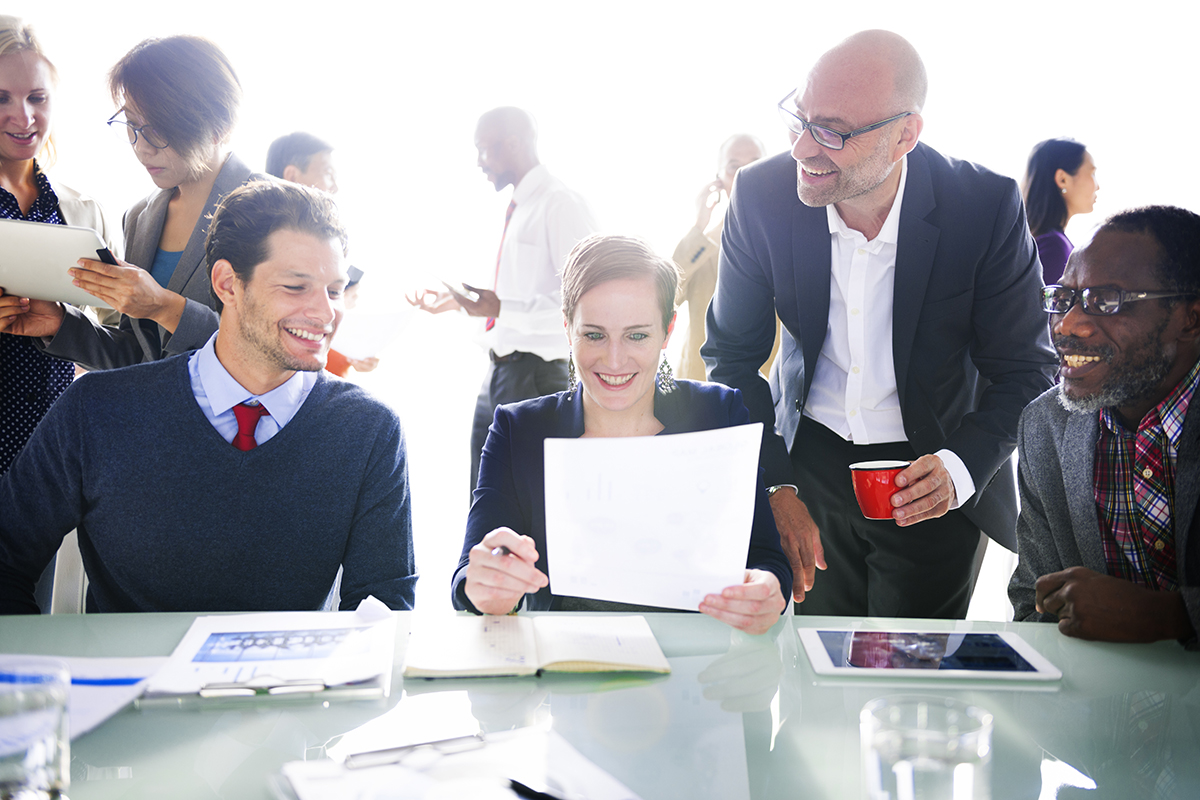 Diverse team smiling over documents at a bright office meeting.