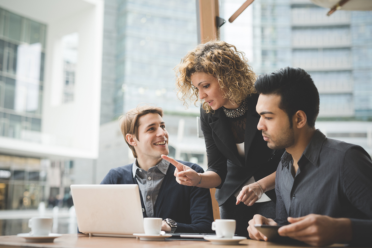 Three professionals discussing over a laptop in a bright office setting.