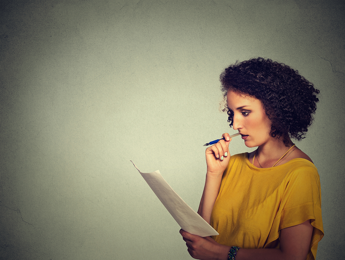 Thoughtful woman with curly hair contemplating while holding pen and paper.