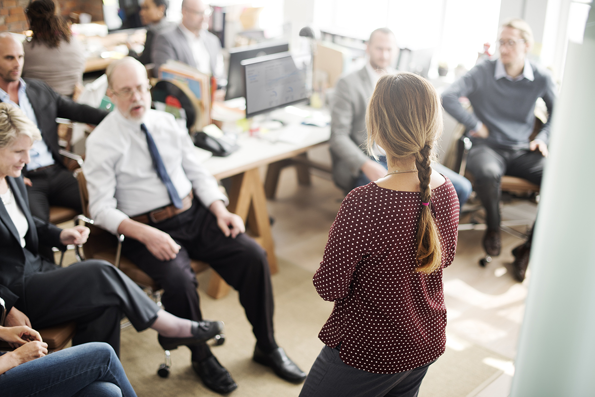 Diverse office staff attentively listening to a female colleague giving a presentation.