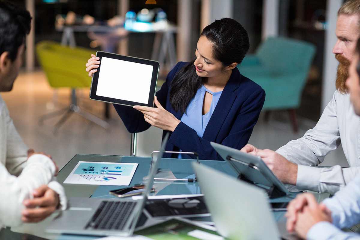 Businesswoman presenting on tablet to colleagues at a modern office.