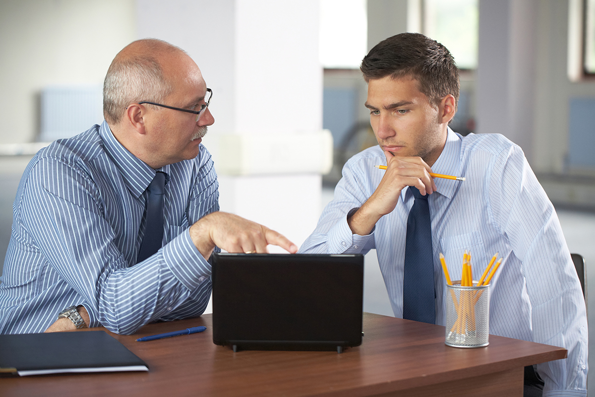 Two businessmen in a discussion, one explaining something on a tablet to a pensive colleague.