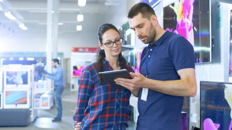 Salesperson assisting a customer with a tablet in an electronics store.