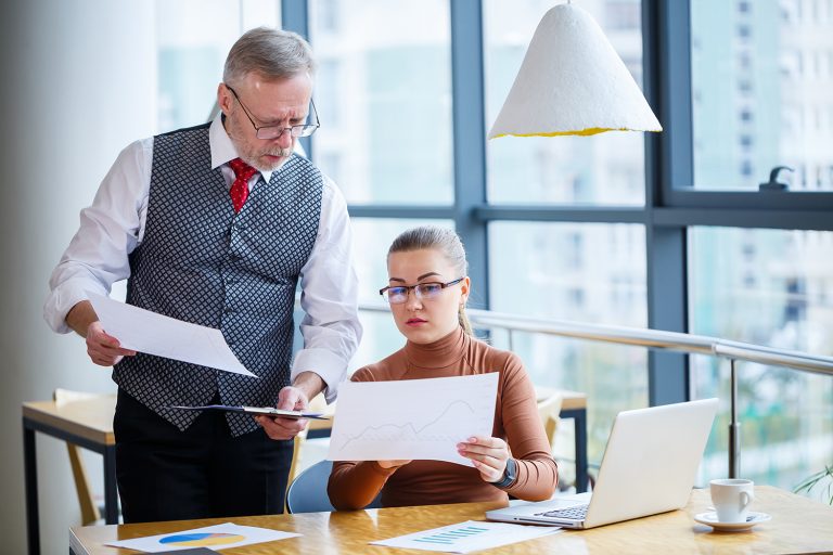 Senior businessman discussing documents with a young female colleague in a modern office.