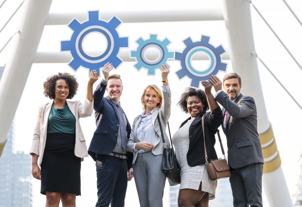 Diverse team of professionals holding up gear icons symbolizing collaboration and teamwork.