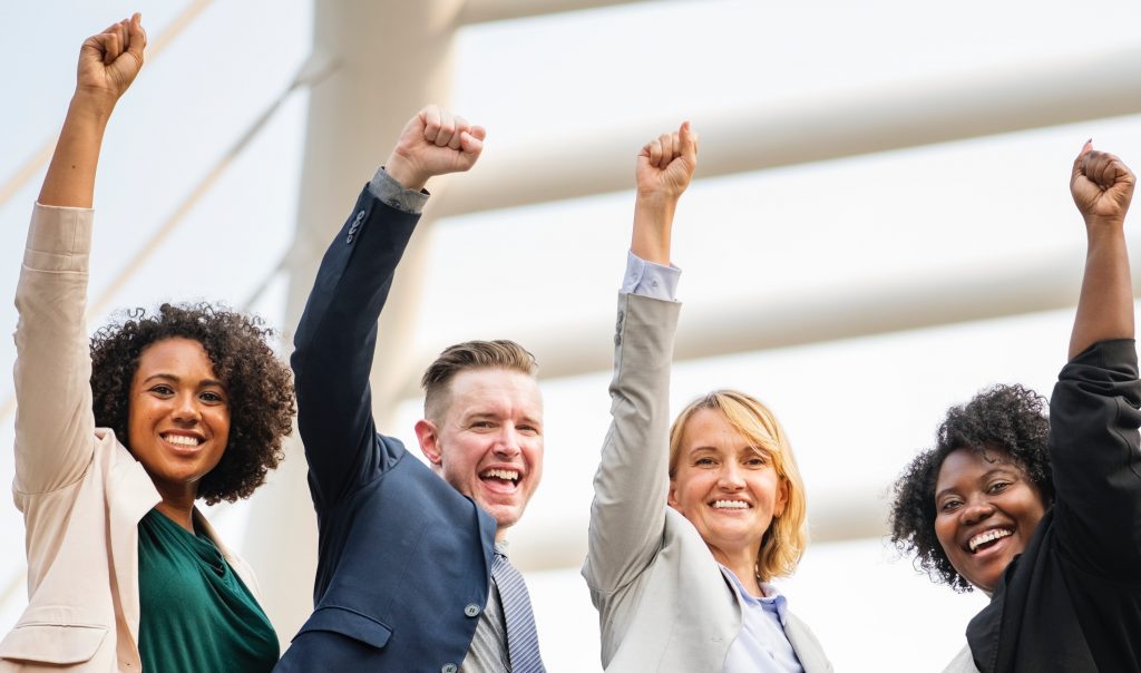 Diverse group of professionals celebrating success with raised fists.