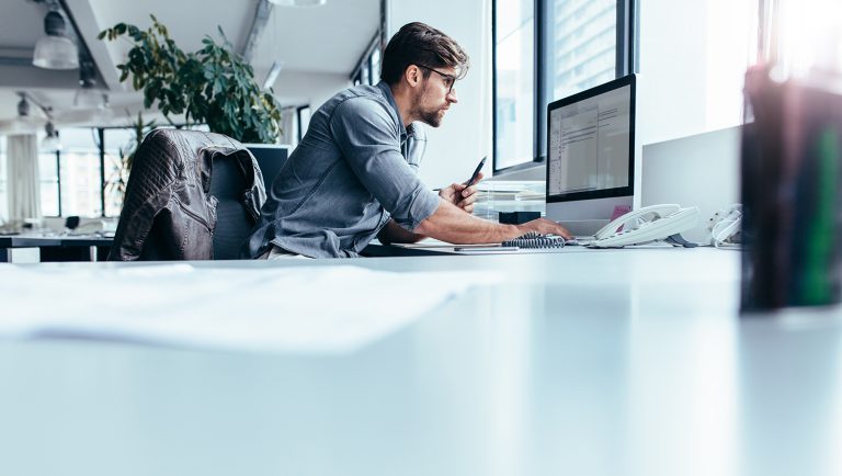 Man working intently at a computer in a modern office with large windows.