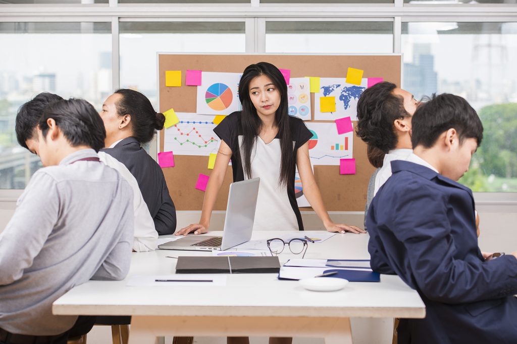 Focused team with one woman standing at a brainstorming session with sticky notes and charts.