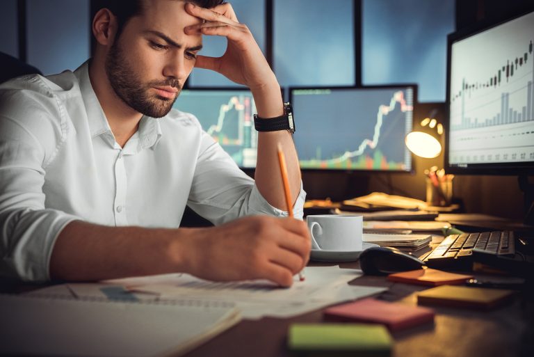 Stressed businessman working late, analyzing charts and graphs on multiple computer screens.