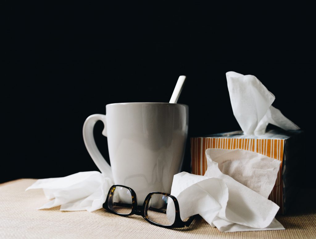 Hot tea mug, tissue box, and glasses, suggesting cold or flu treatment and care.