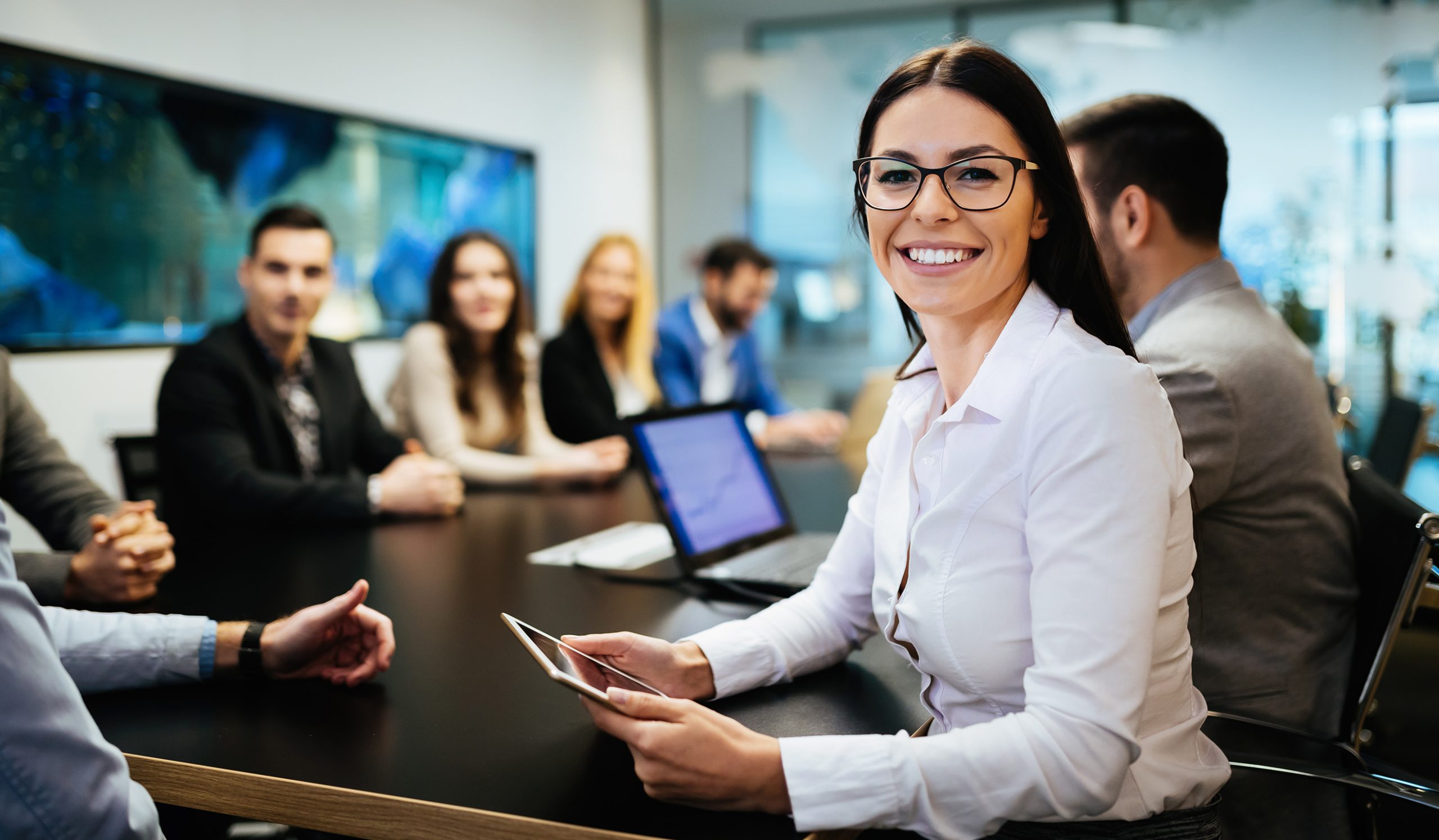 Confident businesswoman using tablet in a meeting with colleagues in background.