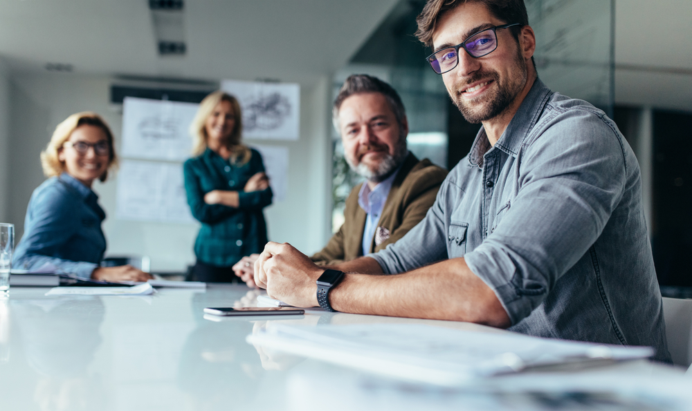 Confident business professionals smiling in a meeting, with focus on man in glasses.