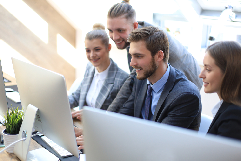 Four professionals smiling at a computer, collaborating on a project.