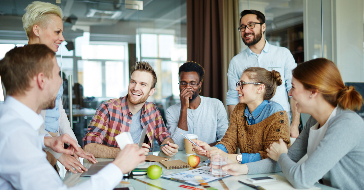 Diverse group of smiling colleagues in a meeting with documents and a laptop.