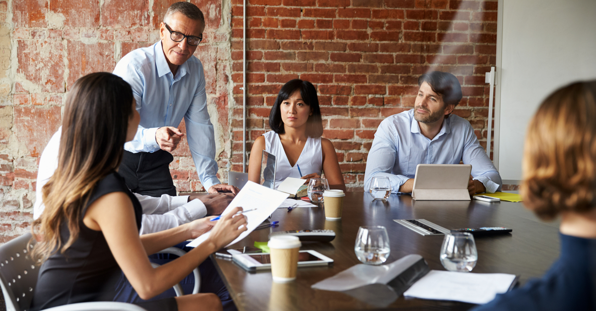 Senior manager explaining documents to attentive coworkers in a meeting.