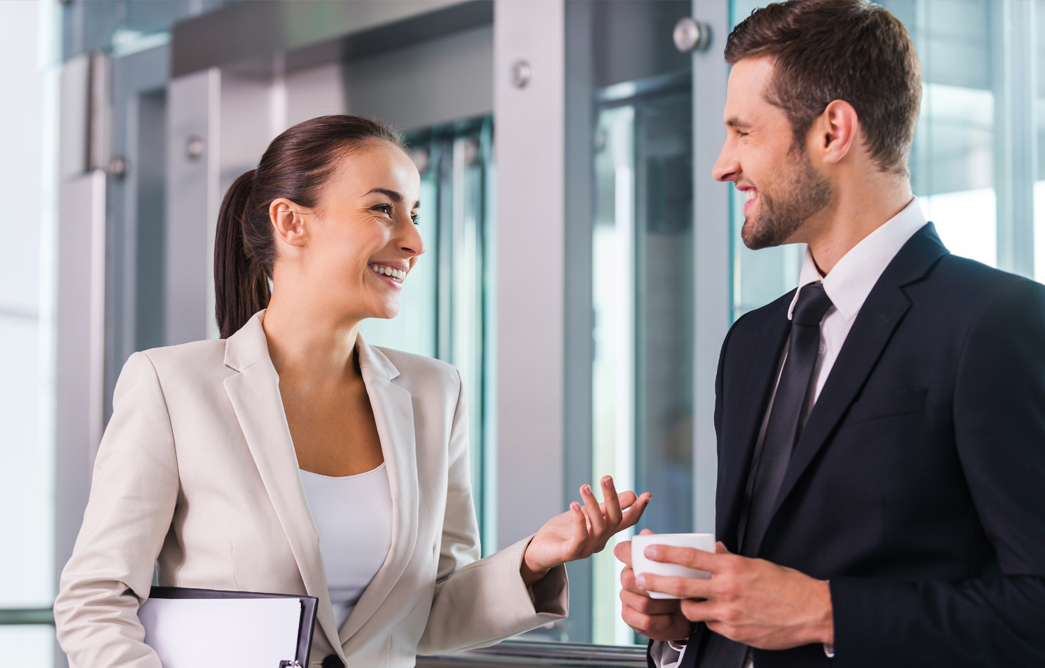 Professional man and woman happily conversing with coffee and documents in hand.