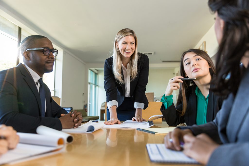 Smiling female leader engaging with diverse team during a meeting in a modern office.