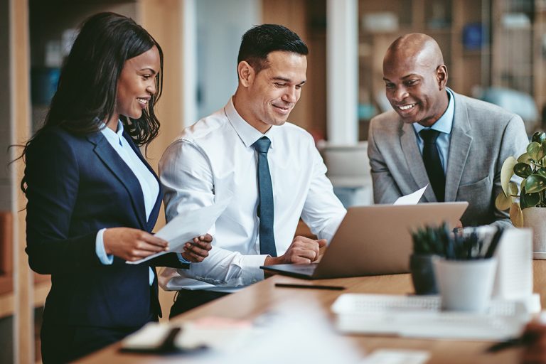 Diverse group of business professionals in suits collaborating on a laptop.