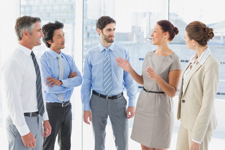 Group of professionals engaged in a conversation, with a woman leading the discussion in a bright office.