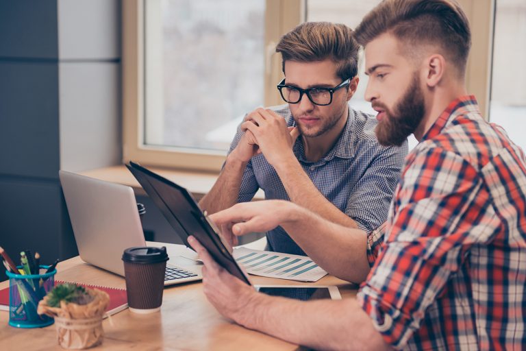 Two men reviewing data on tablet and laptop in modern office setting.