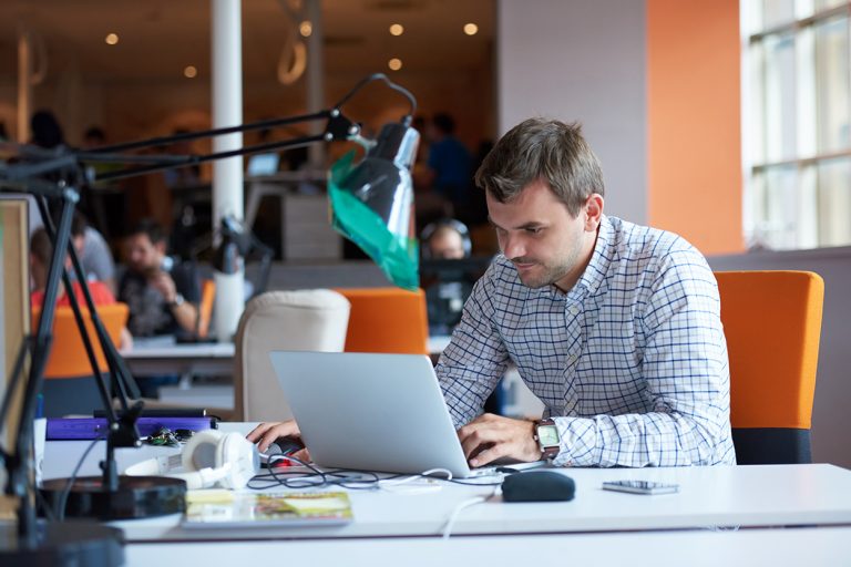 Focused young man working on a laptop at a busy, vibrant coworking space with bright orange accents.